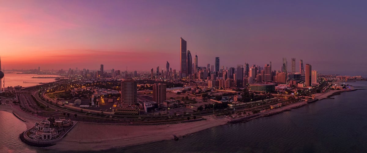 A city skyline at sunset with modern skyscrapers and a waterfront promenade.