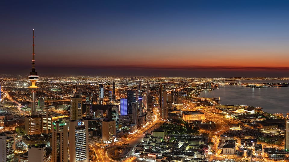 A cityscape at dusk with a prominent tower and a waterfront.