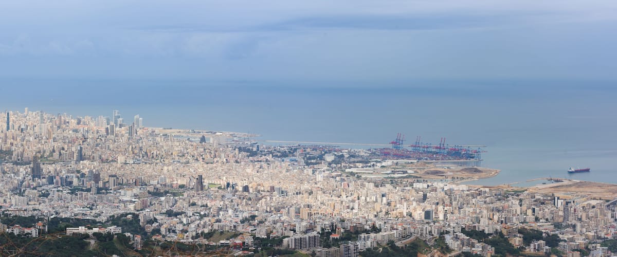 A coastal cityscape with dense urban development, a port with cranes, and a large body of water.