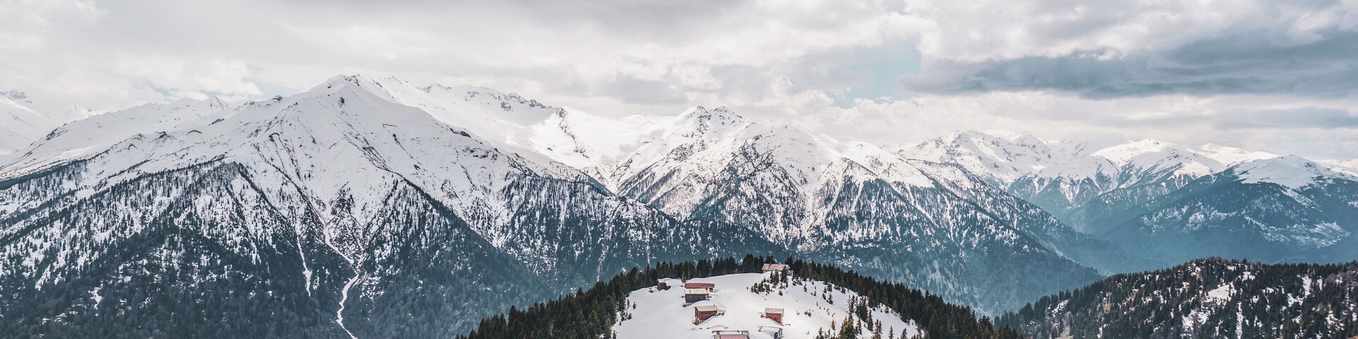 Uma aldeia montanhosa coberta de neve, com casas de madeira e céu claro.