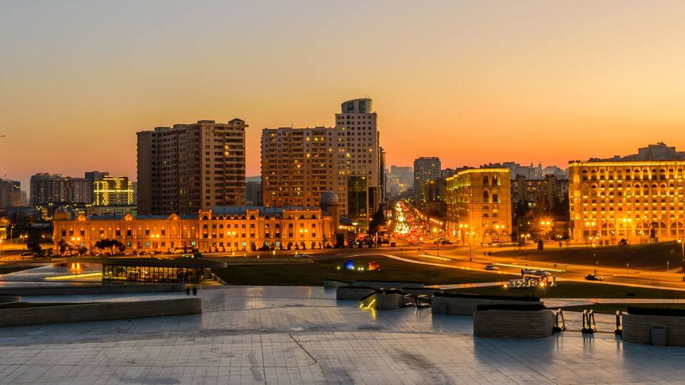 A cityscape at dusk with illuminated buildings and a modern architectural structure.