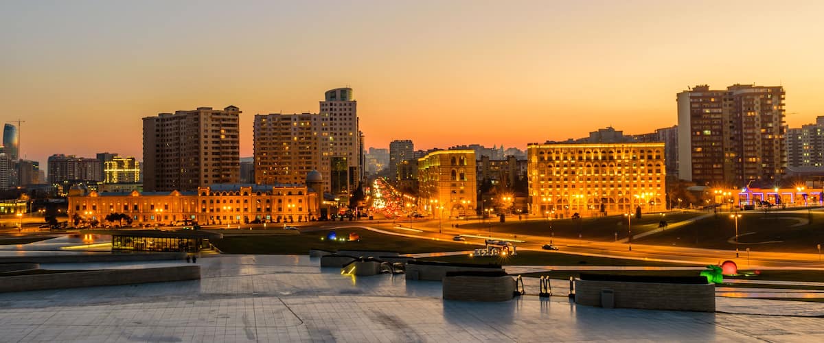 A cityscape at dusk with illuminated buildings and a modern architectural structure.