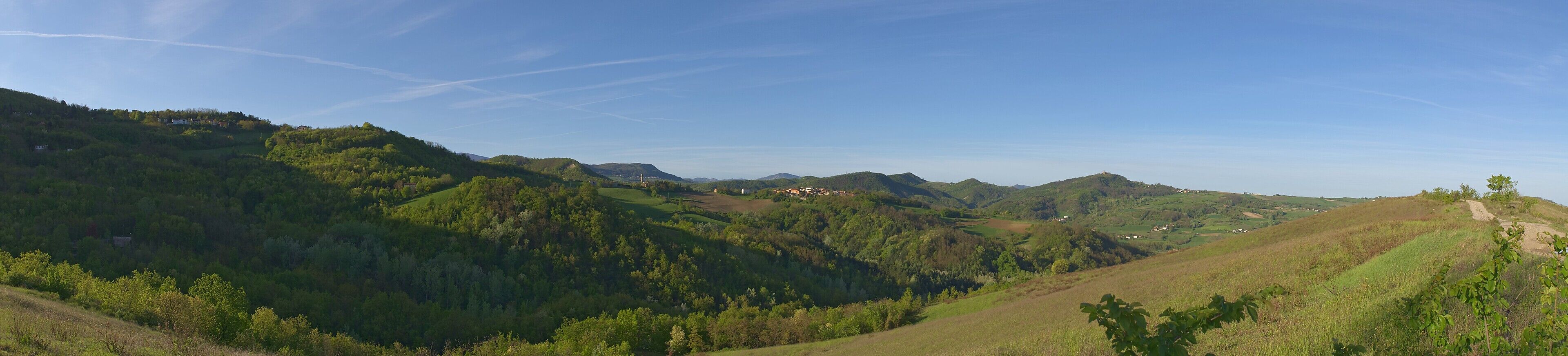 A valley with rolling hills, scattered houses, and a clear blue sky.