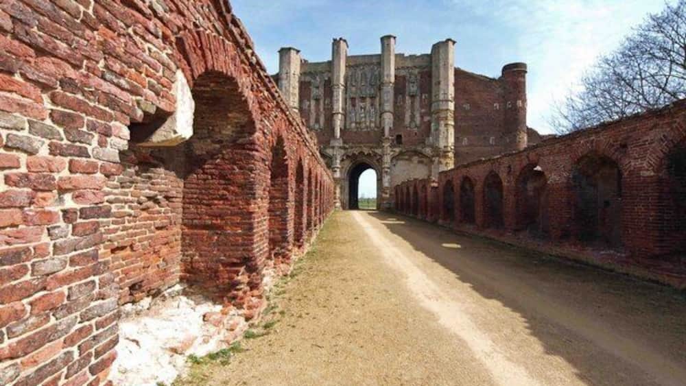 A brick pathway leading to a historic building with arched walkways and a large gate.
