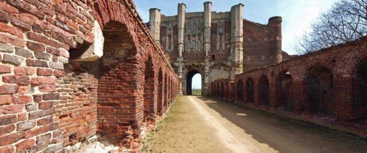 Een pad van baksteen leidt naar een historisch gebouw met booggangen en een grote poort.