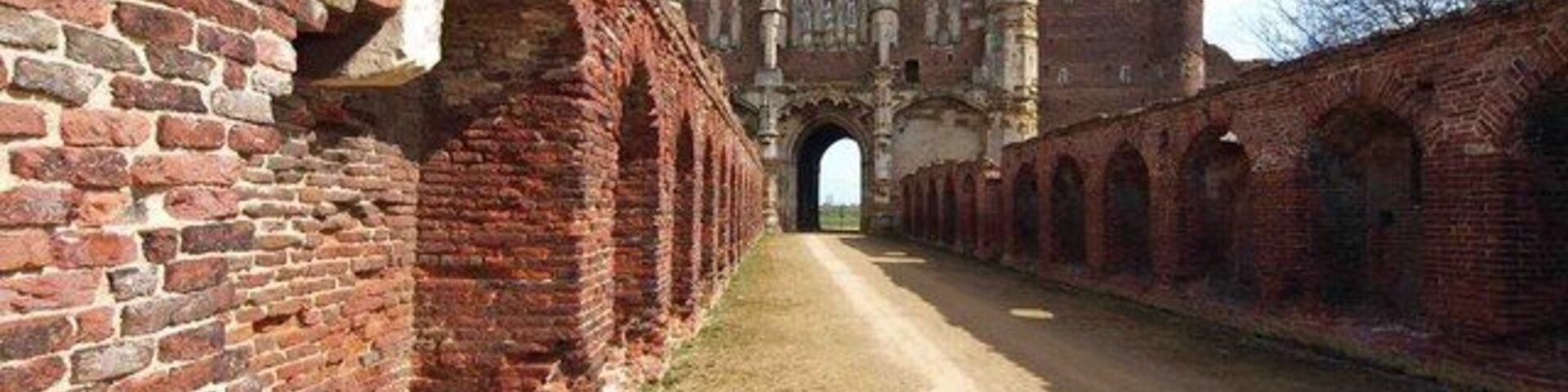 Uma trilha de tijolos que leva a um edifício histórico com arcadas e um grande portão.