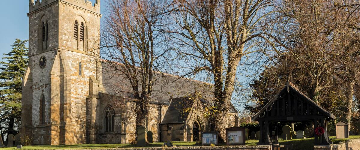 A historic church with a tall tower and a large tree in front.