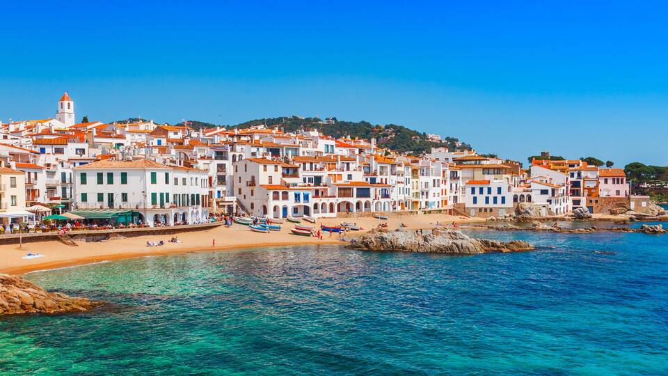 A coastal town with white buildings, a beach, and clear blue waters.