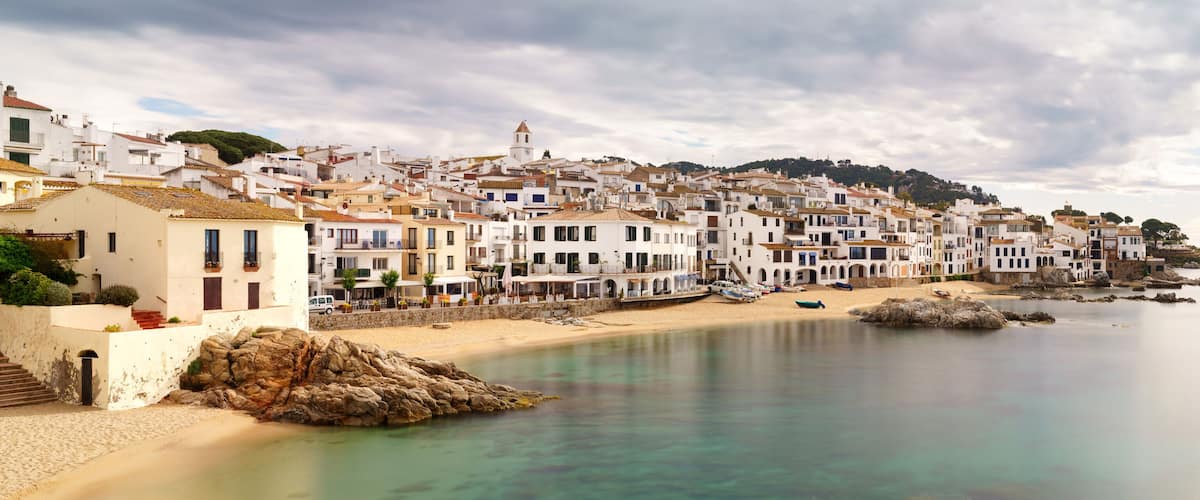A coastal town with white buildings, a sandy beach, and rocky outcrops.