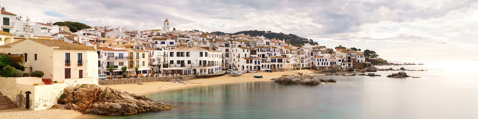 A coastal town with white buildings, a sandy beach, and rocky outcrops.