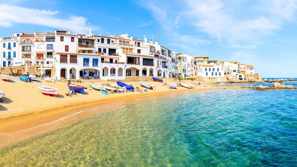 A coastal town with white buildings, a sandy beach, and boats.