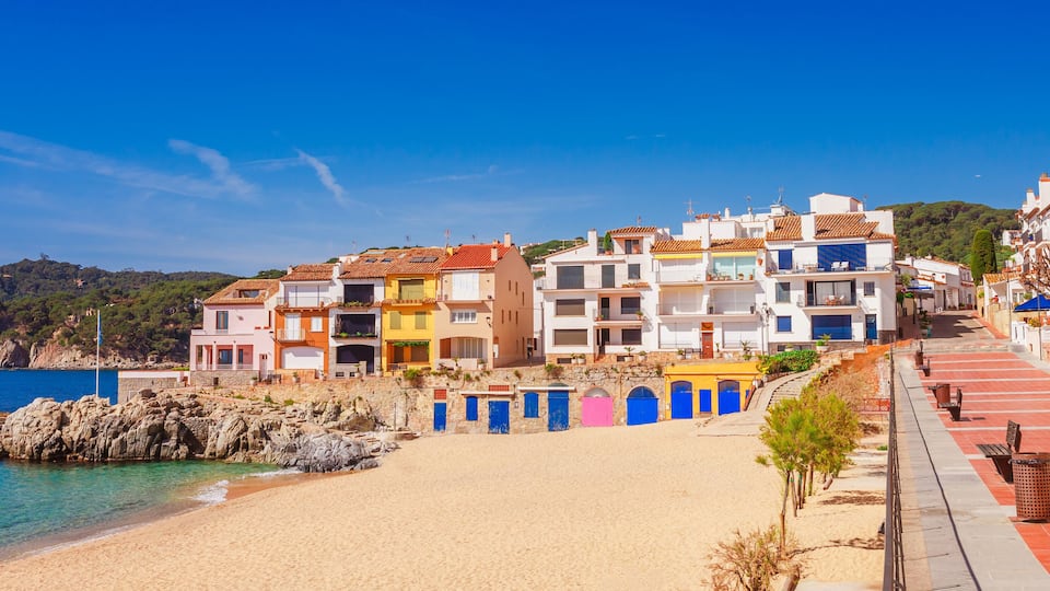 A coastal town with colorful buildings, a sandy beach, and a rocky shoreline.