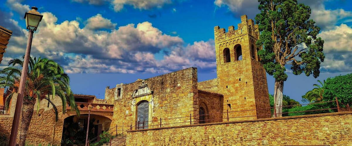 A historic stone building with a tower, palm trees, and a clear sky.