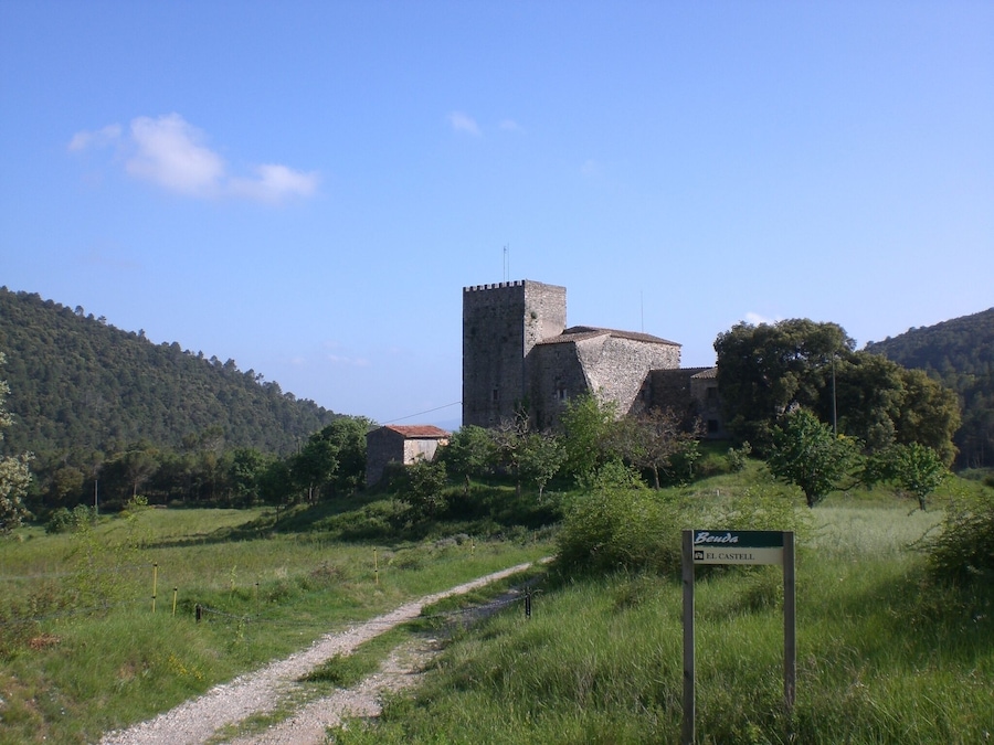 Un castillo medieval rodeado de colinas verdes exuberantes y un cielo azul despejado.
