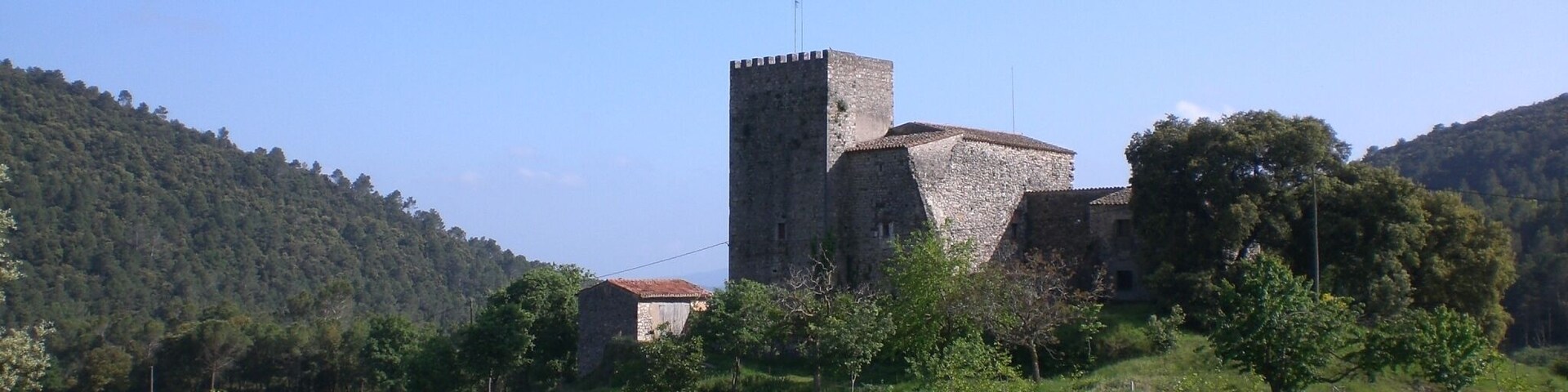 Eine mittelalterliche Burg, umgeben von üppigen grünen Hügeln und wolkenlosem, blauem Himmel.