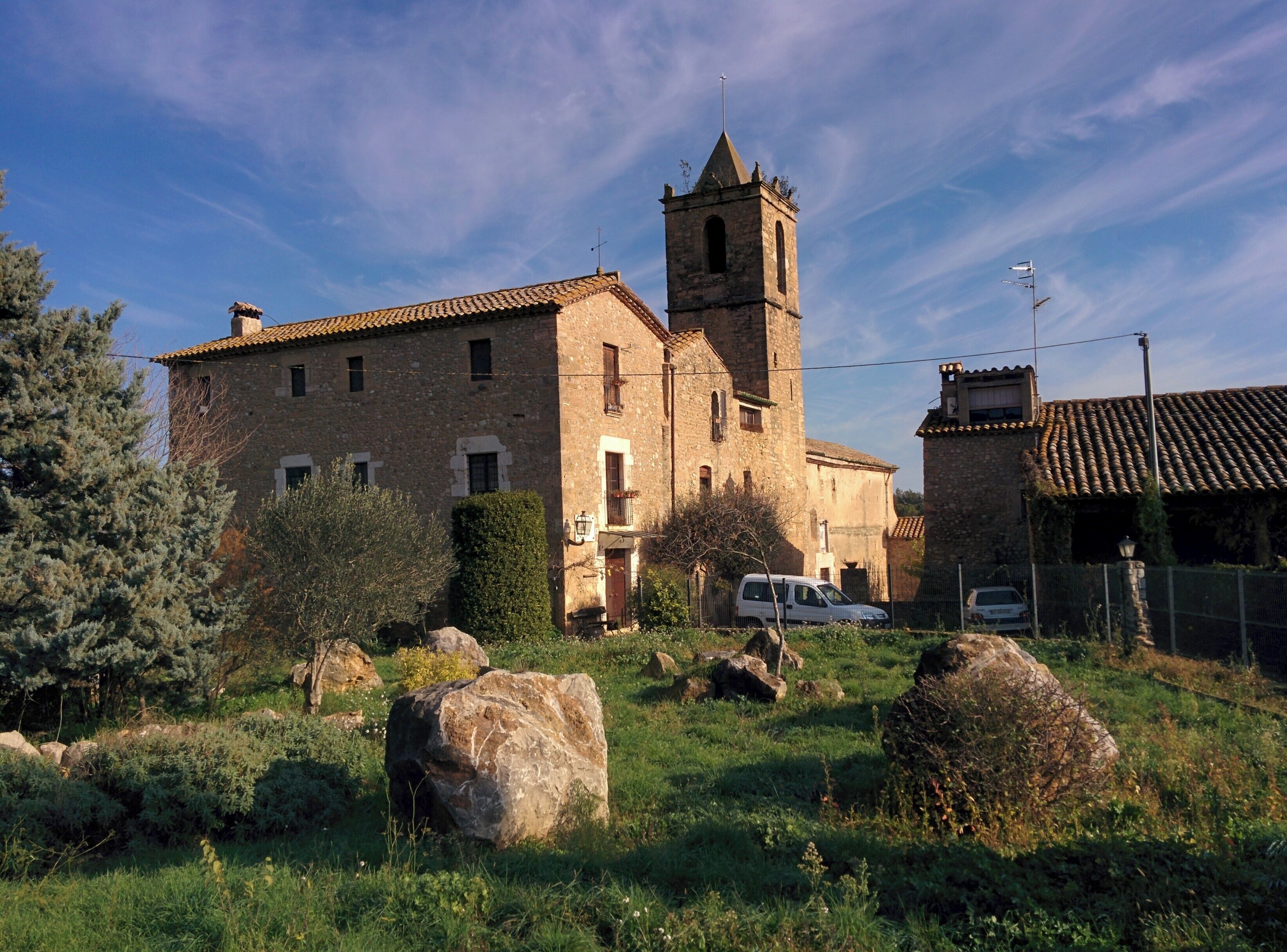 A stone church with a bell tower, surrounded by greenery and rocks.
