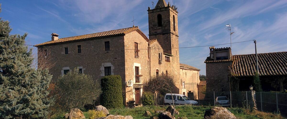 A stone church with a bell tower, surrounded by greenery and rocks.