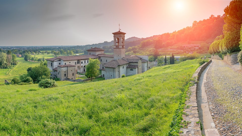 A historic building complex with a bell tower, surrounded by lush green fields and a stone pathway.