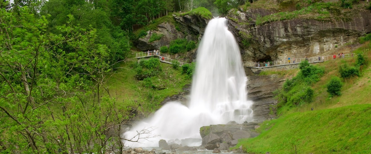 A waterfall cascading down a rocky cliff into a river below, surrounded by lush greenery and a viewing platform.