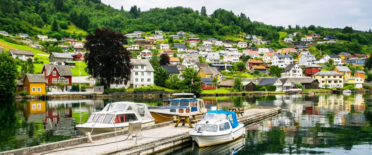 Un village au bord d’un lac, avec des bateaux amarrés à un quai, entouré d’une végétation luxuriante et de maisons aux couleurs vives.