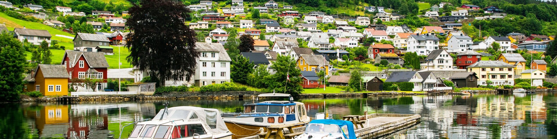 Un pueblo junto al lago con barcos amarrados en un muelle, rodeado de abundante vegetación y casas coloridas.