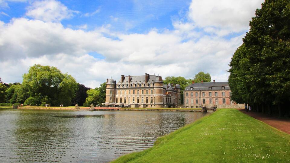 A large historic building with a moat, surrounded by lush greenery and a clear sky.