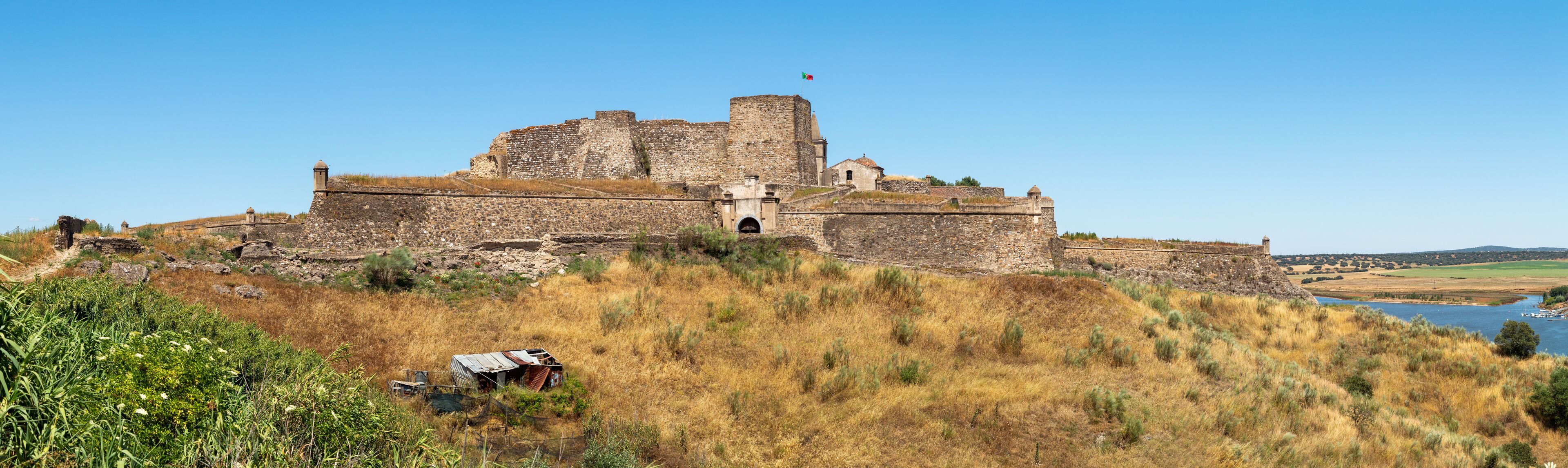 A historic stone castle on a hill overlooking a river.