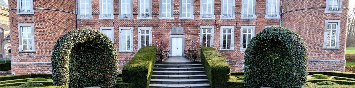 Main facade of 16th century Alden Biesen castle, circular towers, staircase, brick walls, windows, gable roof and bushes, cloudy day in Bilzen, Limburg, Belgium