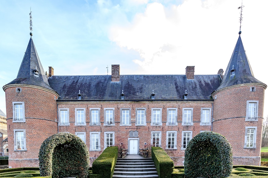 Main facade of 16th century Alden Biesen castle, circular towers, staircase, brick walls, windows, gable roof and bushes, cloudy day in Bilzen, Limburg, Belgium