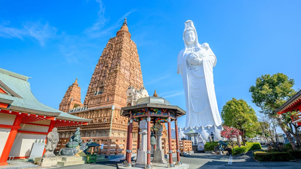 A large white statue, a traditional temple with a tiered tower, and a small pavilion with colorful stained glass.