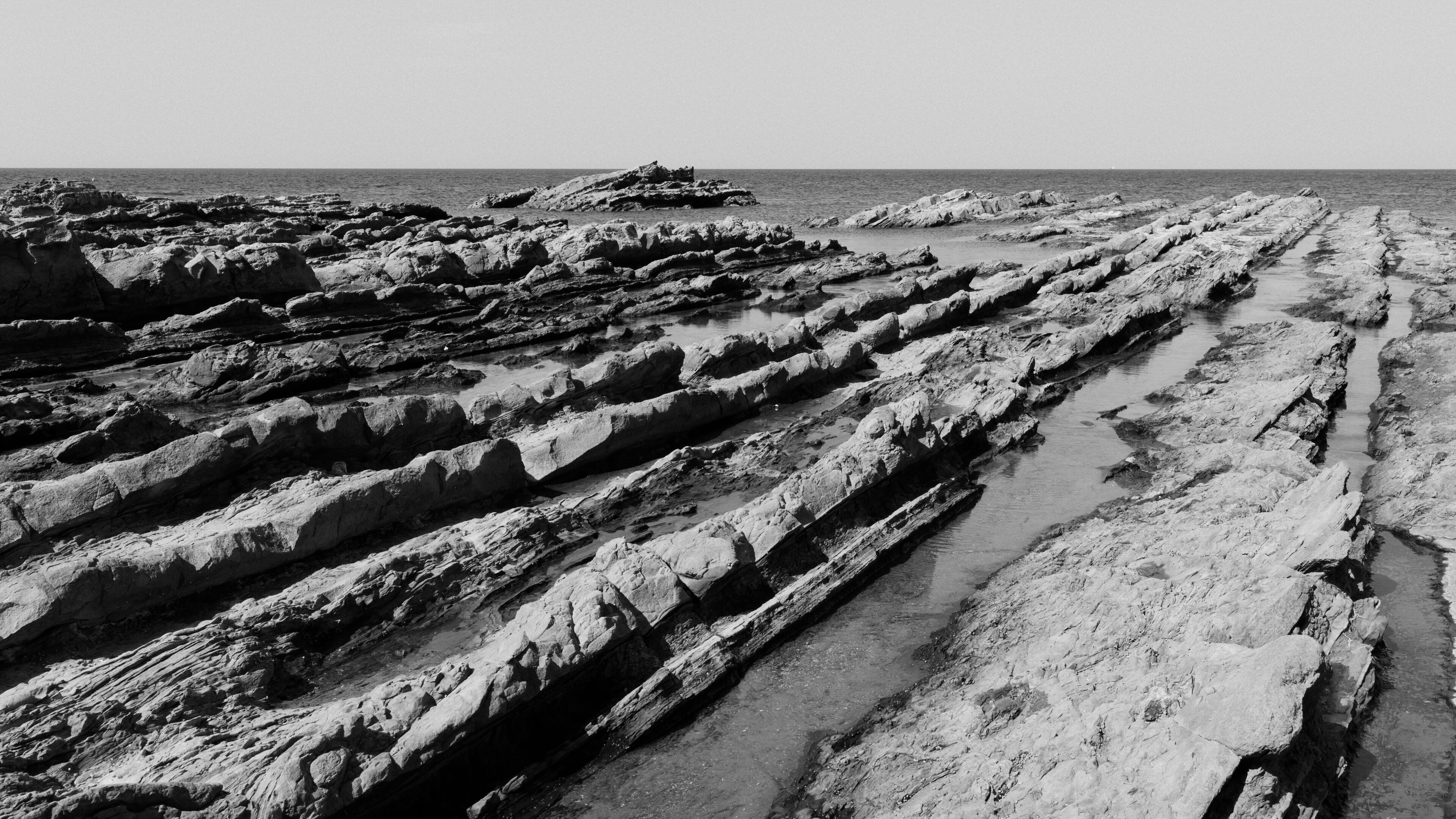 A rocky coastal landscape with layered sedimentary formations and a narrow water channel.