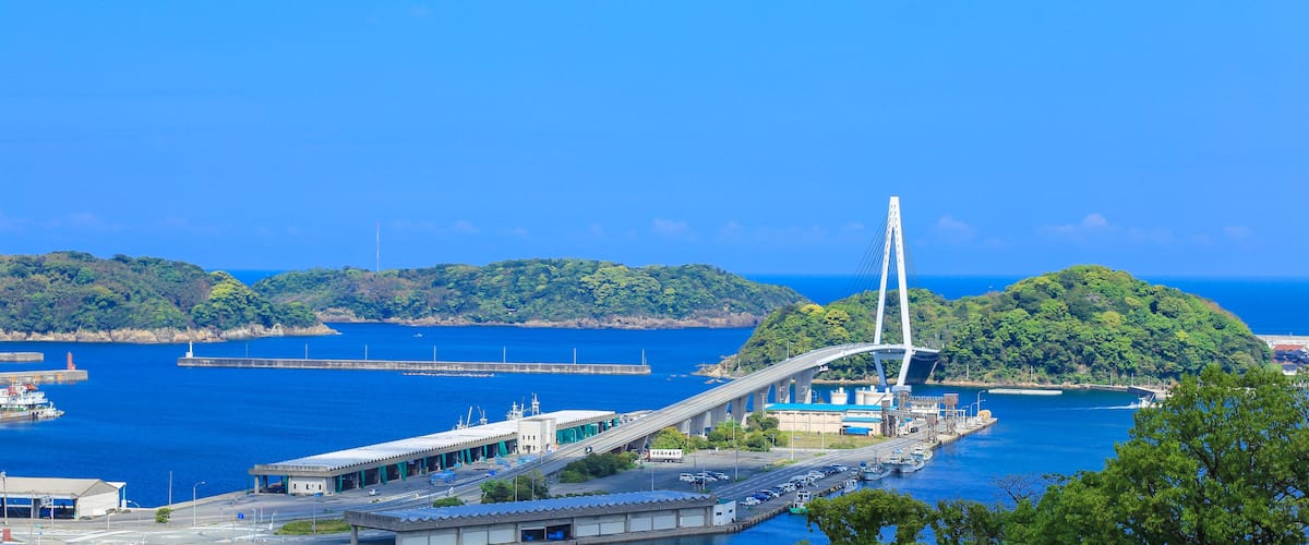 A cable-stayed bridge, a coastal road, and a harbor with boats.