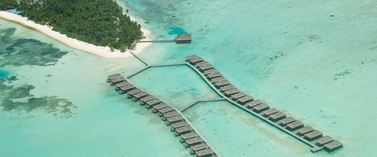 Vista aérea de um resort com bangalôs sobre a água conectados por passarelas.