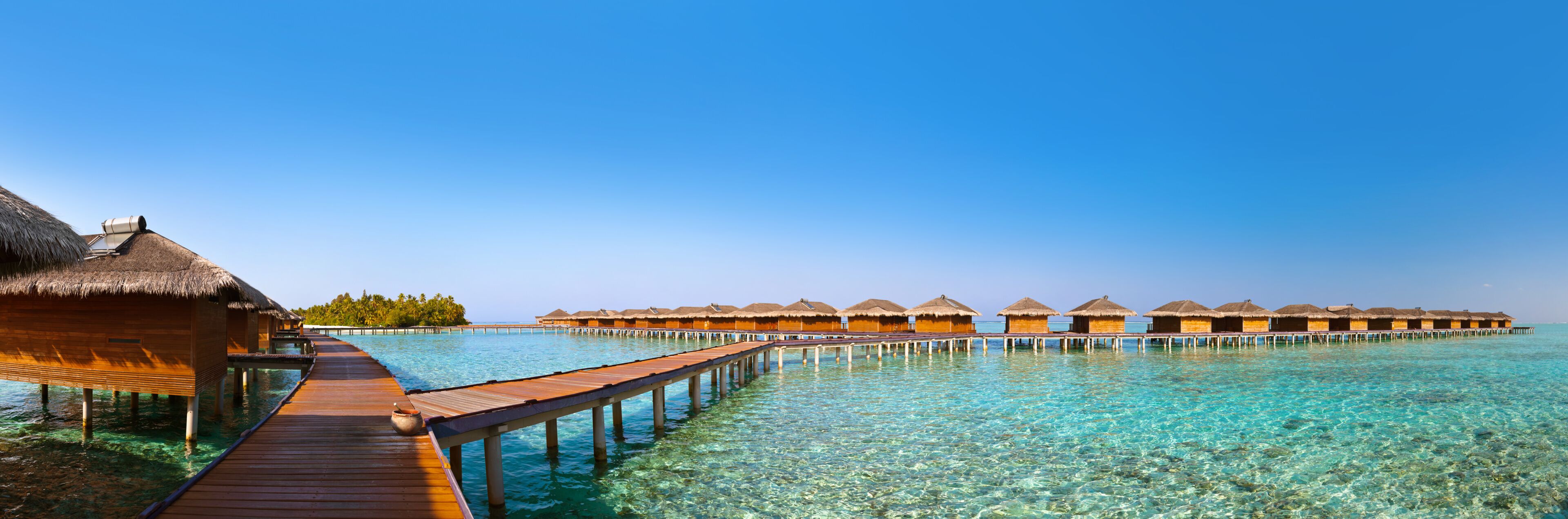 Overwater bungalows connected by wooden walkways over clear turquoise water.