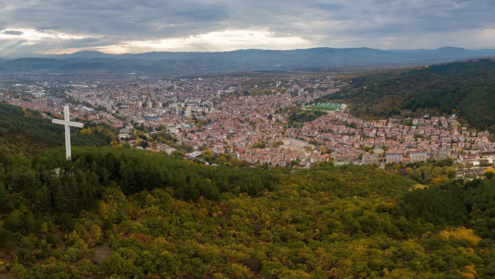 Un paysage urbain avec une grande croix qui se dresse sur une colline surplombant une zone densément peuplée.