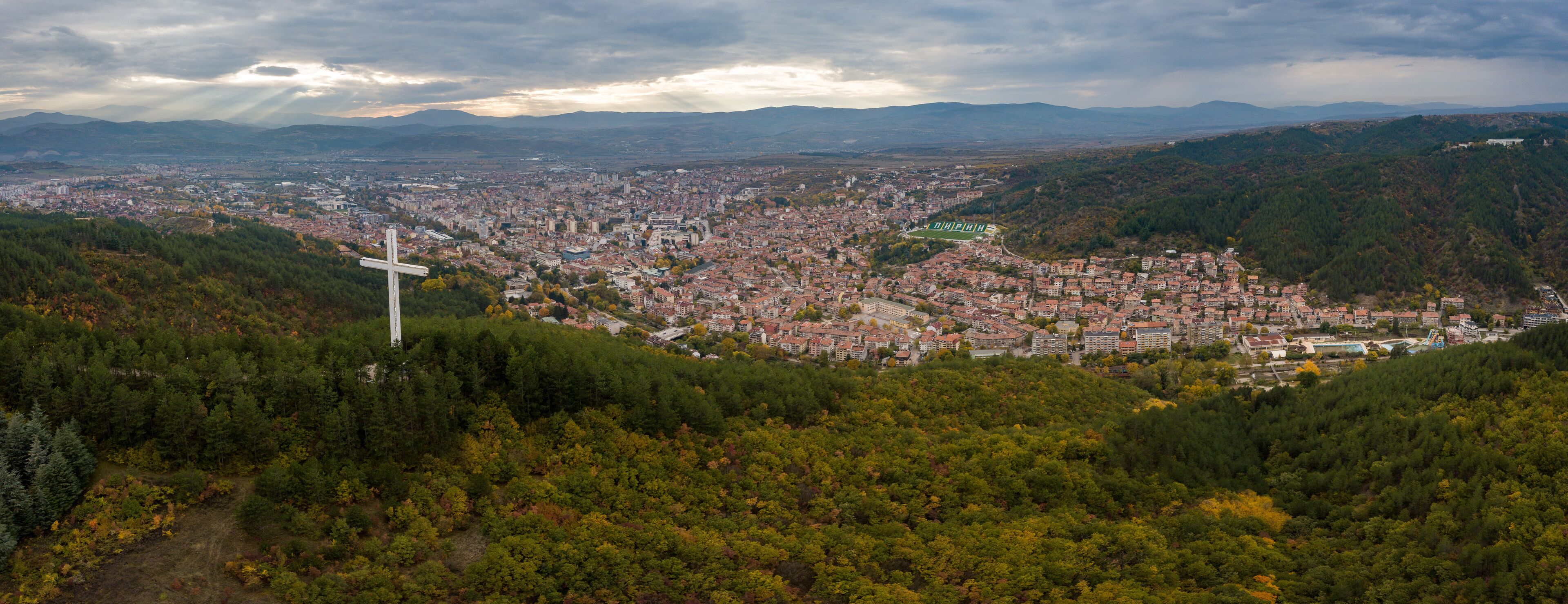 A cityscape with a prominent cross on a hill overlooking a densely populated area.