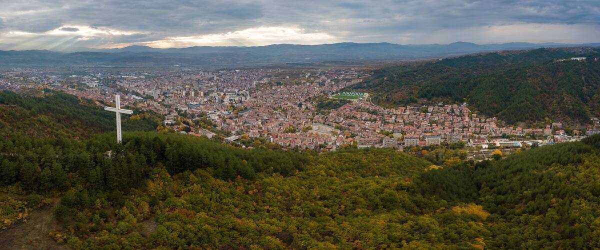 A cityscape with a prominent cross on a hill overlooking a densely populated area.