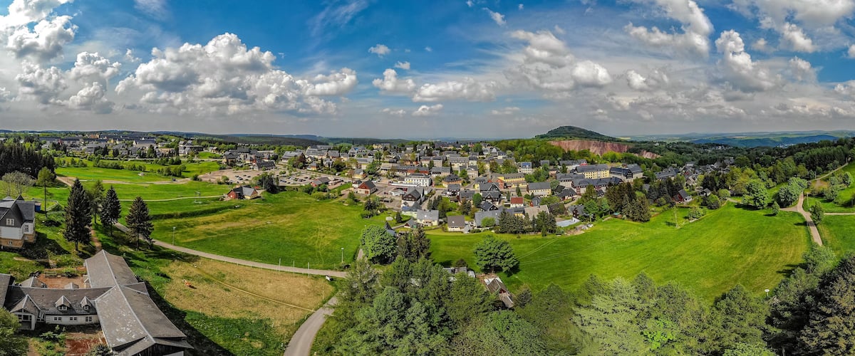 A town with a central green park, surrounded by houses and a hill in the background.