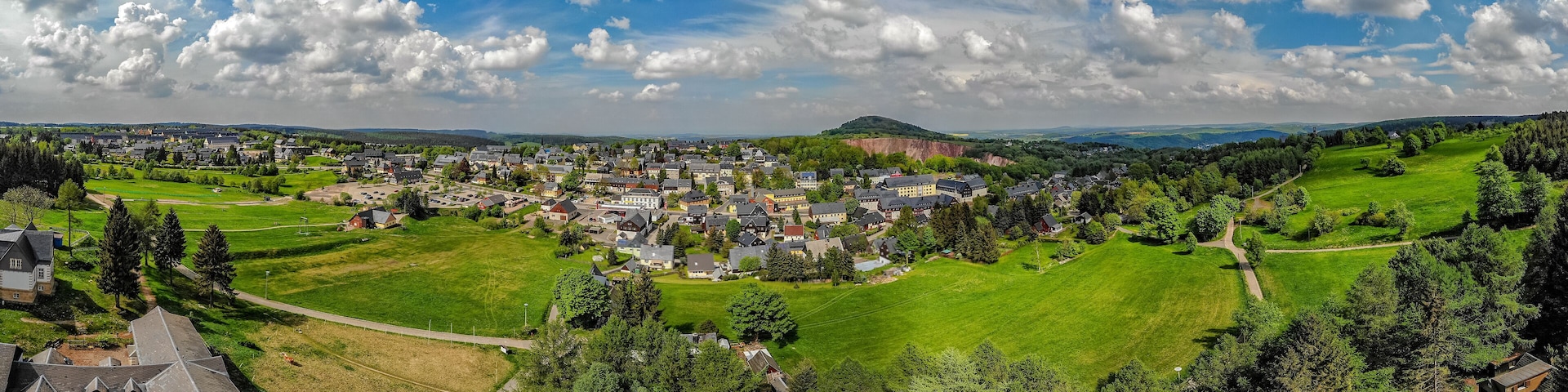 A town with a central green park, surrounded by houses and a hill in the background.