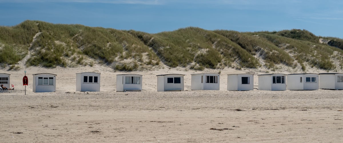 A row of beach huts with a dune in the background.