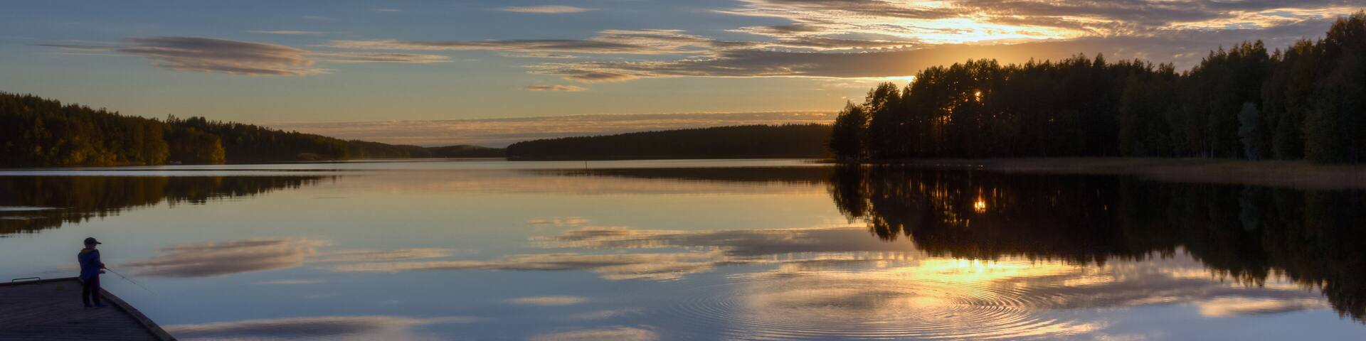 A calm lake at sunset with a wooden dock and a person fishing.