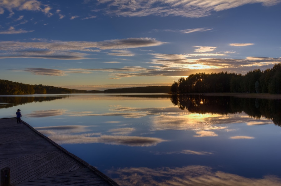 A calm lake at sunset with a wooden dock and a person fishing.