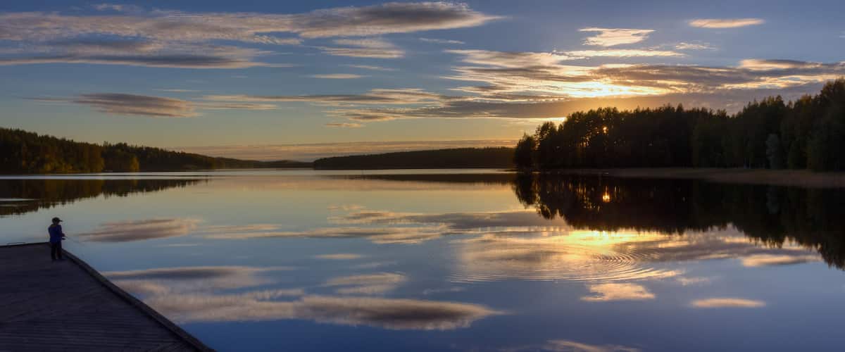A calm lake at sunset with a wooden dock and a person fishing.