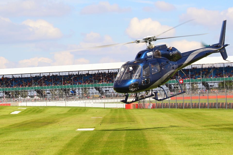 A blue helicopter hovering over a sports stadium with a crowd in the stands.