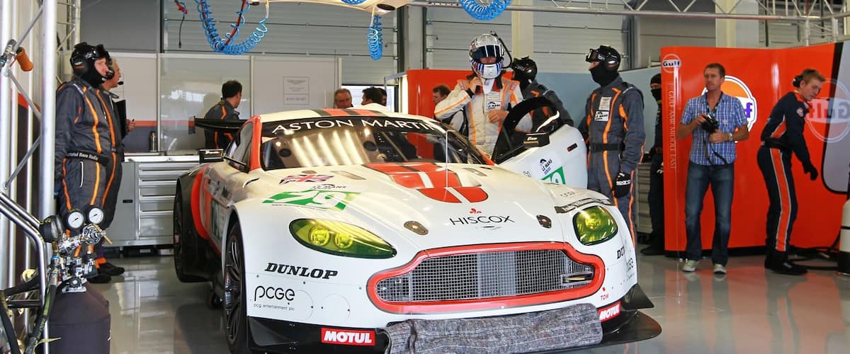 A race car in a garage with various logos and a team of mechanics.