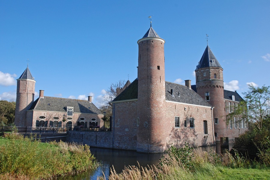 Een historisch kasteel van baksteen met twee torens, een gracht en een brug.