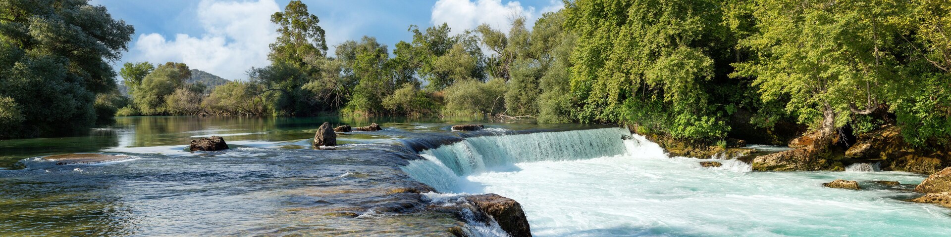 A waterfall cascading over rocks in a forested area with a river flowing below.