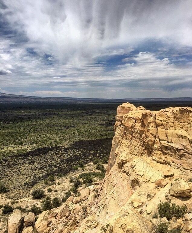 A rocky cliff edge overlooking a vast, flat landscape with sparse vegetation.