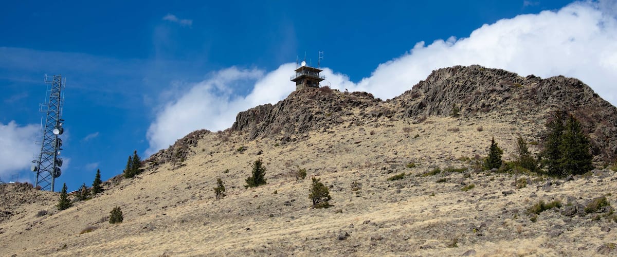 A rocky mountain with sparse vegetation, a small tower, and a cell tower.