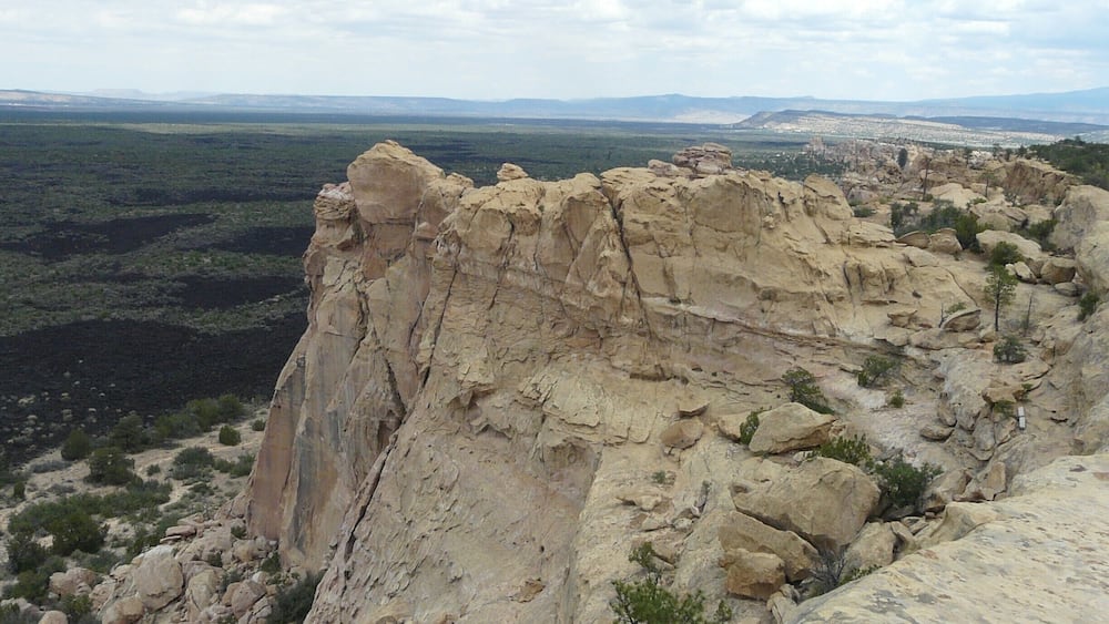 A rugged cliff with sparse vegetation and a distant cityscape.